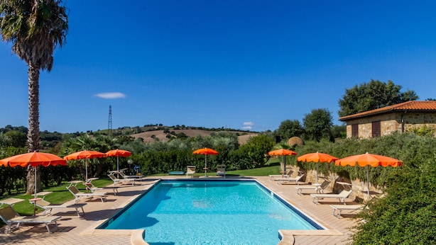 Une piscine entourée de verdure, avec des chaises longues et des parasols, sous un ciel dégagé.