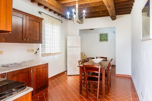 A kitchen with wooden cabinets, a dining table with chairs, a refrigerator, and a chandelier.