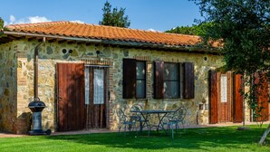 Un bâtiment en pierre avec un toit en tuiles, une porte en bois et une table entourée de chaises au premier plan.