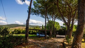 A stone pathway leading to a white car parked under a wooden bridge in a wooded area with hills in the background. - Apartment 'Tartaruga' with Shared Pool, Wi-Fi and Air Conditioning (Montiano)