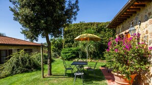 Une terrasse avec une table et des chaises, un pot de fleurs et un mur en pierre.