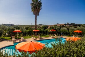 A swimming pool with lounge chairs and umbrellas, surrounded by greenery and hills in the background.