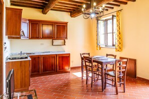 A kitchen with wooden cabinets, a dining table with chairs, a chandelier, and a window with curtains.