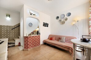 A living room with a sofa, a small table, a kitchen area with a counter, and a staircase with a patterned wall.