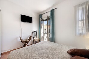 Une chambre à coucher avec un lit, une chaise, un téléviseur et une fenêtre avec des rideaux.