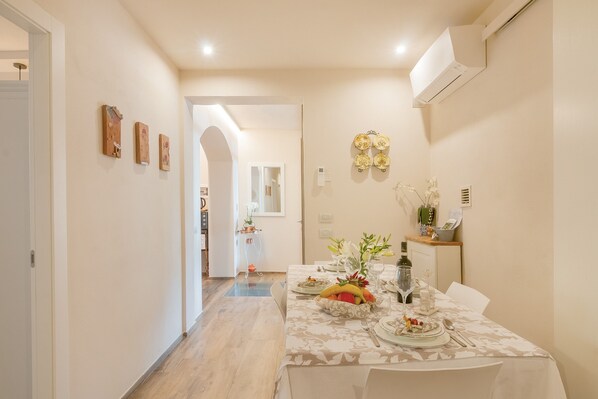 A dining area with a table set for two, a vase with flowers, and a fruit bowl.