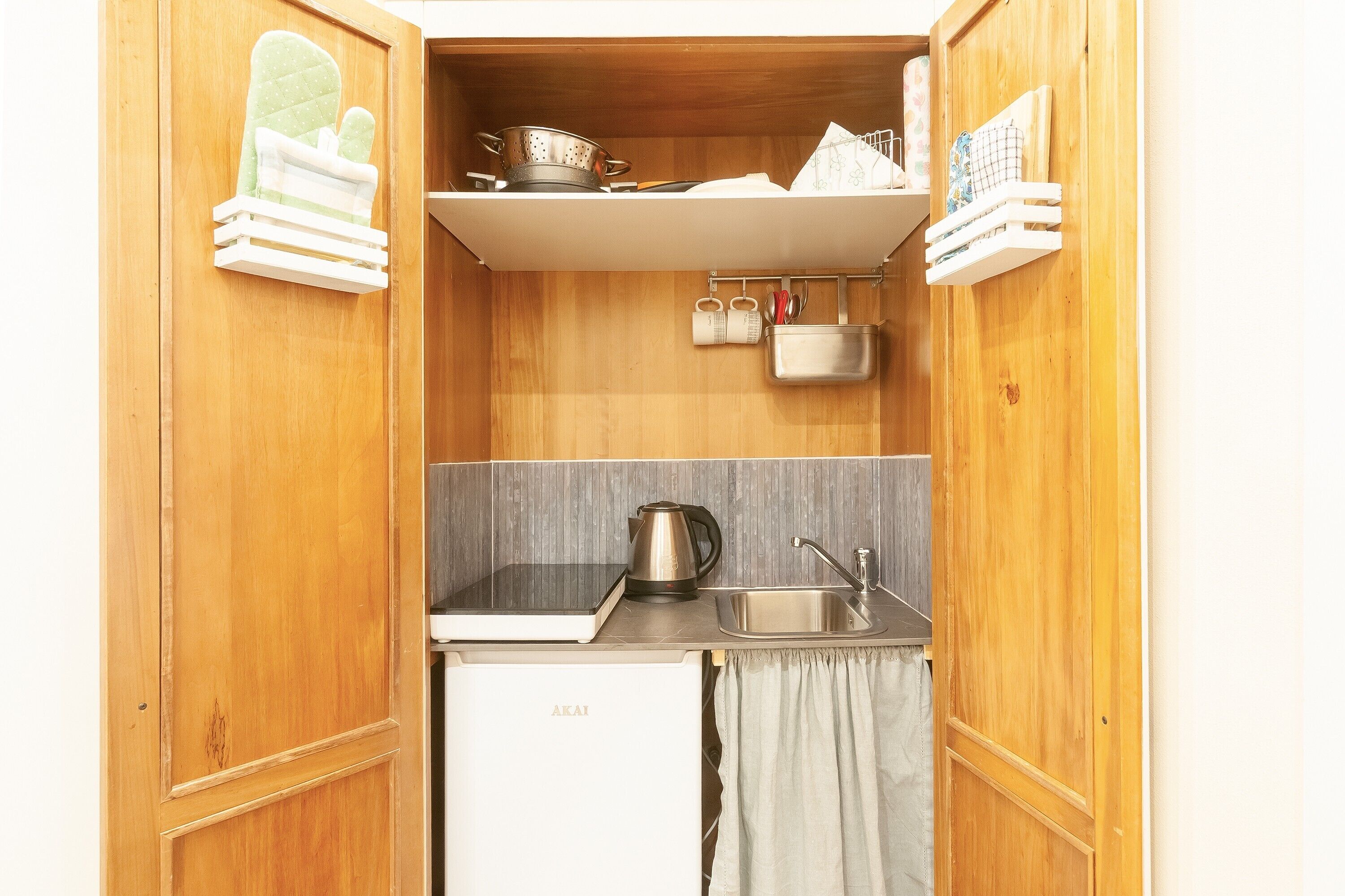 A compact kitchen with wooden cabinetry, a white refrigerator, a sink, and a kettle.