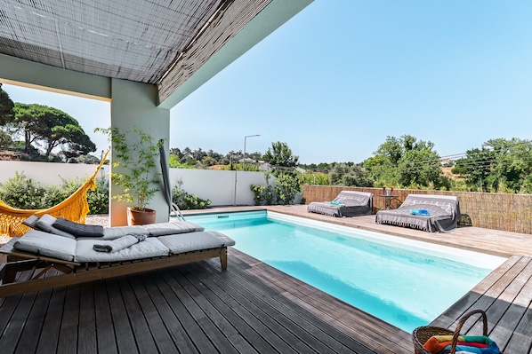 Una terraza de madera con piscina, sillas de descanso y una hamaca.