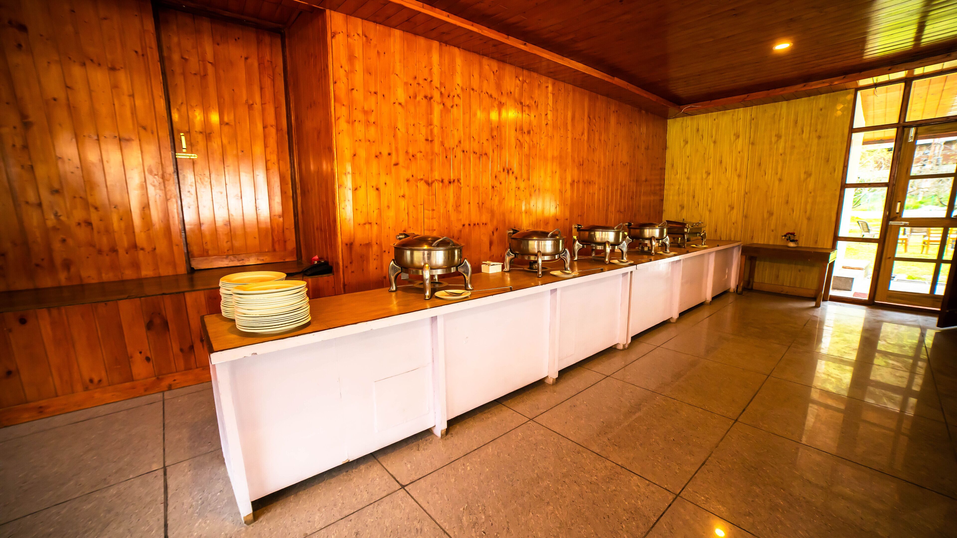 A buffet setup with multiple serving stations, a wooden interior, and a view through a glass door.