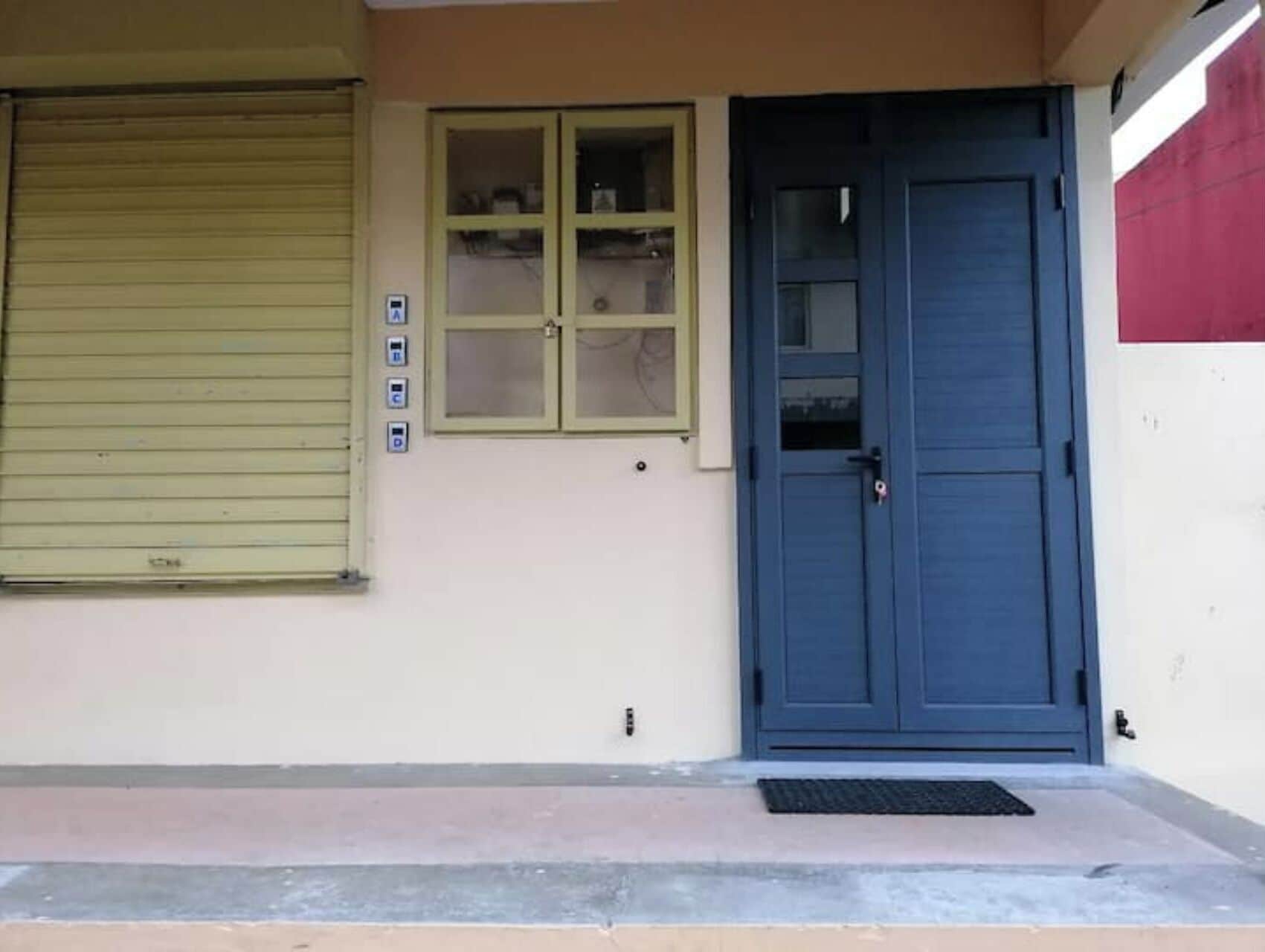 A building with a closed shutter door, a window with a view of the interior, and a small doorbell.