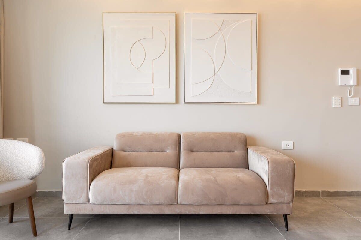 Una sala de estar moderna con un sofá color beige, dos obras de arte abstracto en la pared y un termostato blanco instalado en la pared.