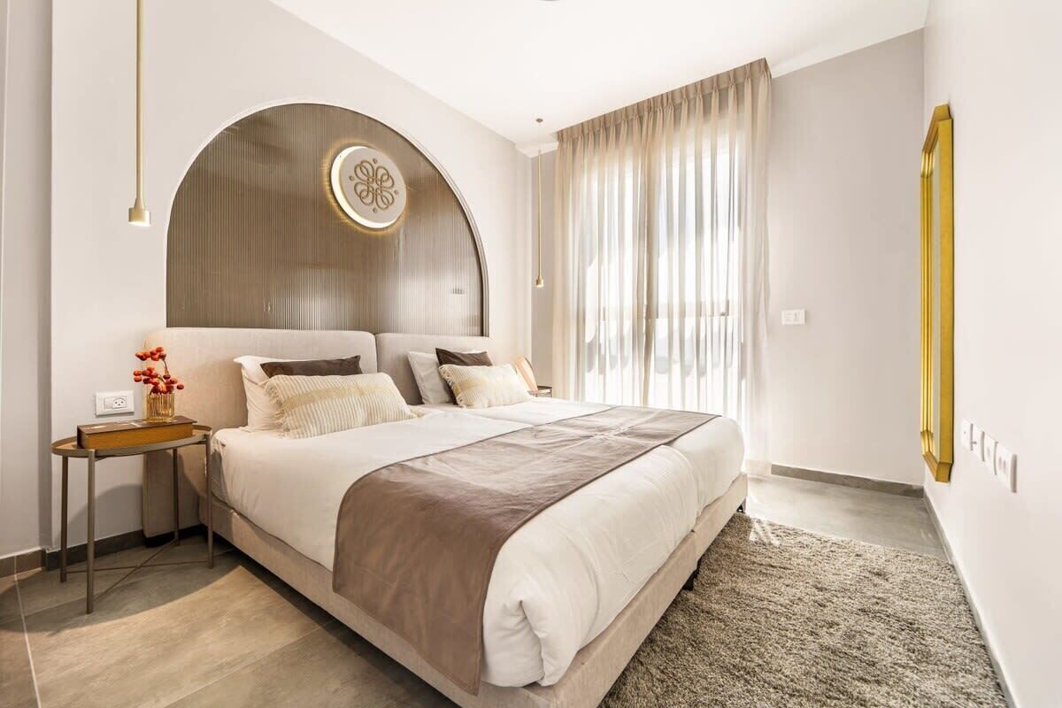 A modern bedroom with a large bed, a bedside table, a decorative wall panel, and a window with curtains.
