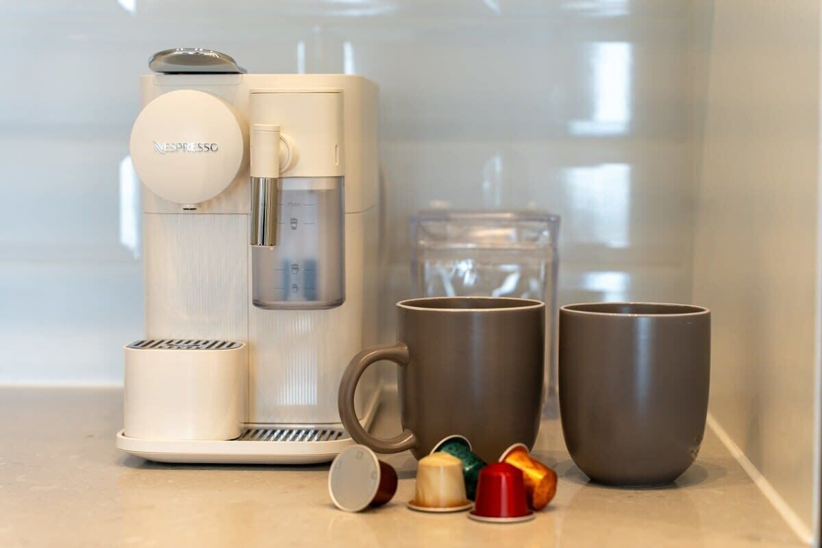 Een Nespresso koffieapparaat, twee mokken en een glas water op een aanrecht.