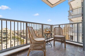 A balcony with wicker chairs and a small table, offering a city view.