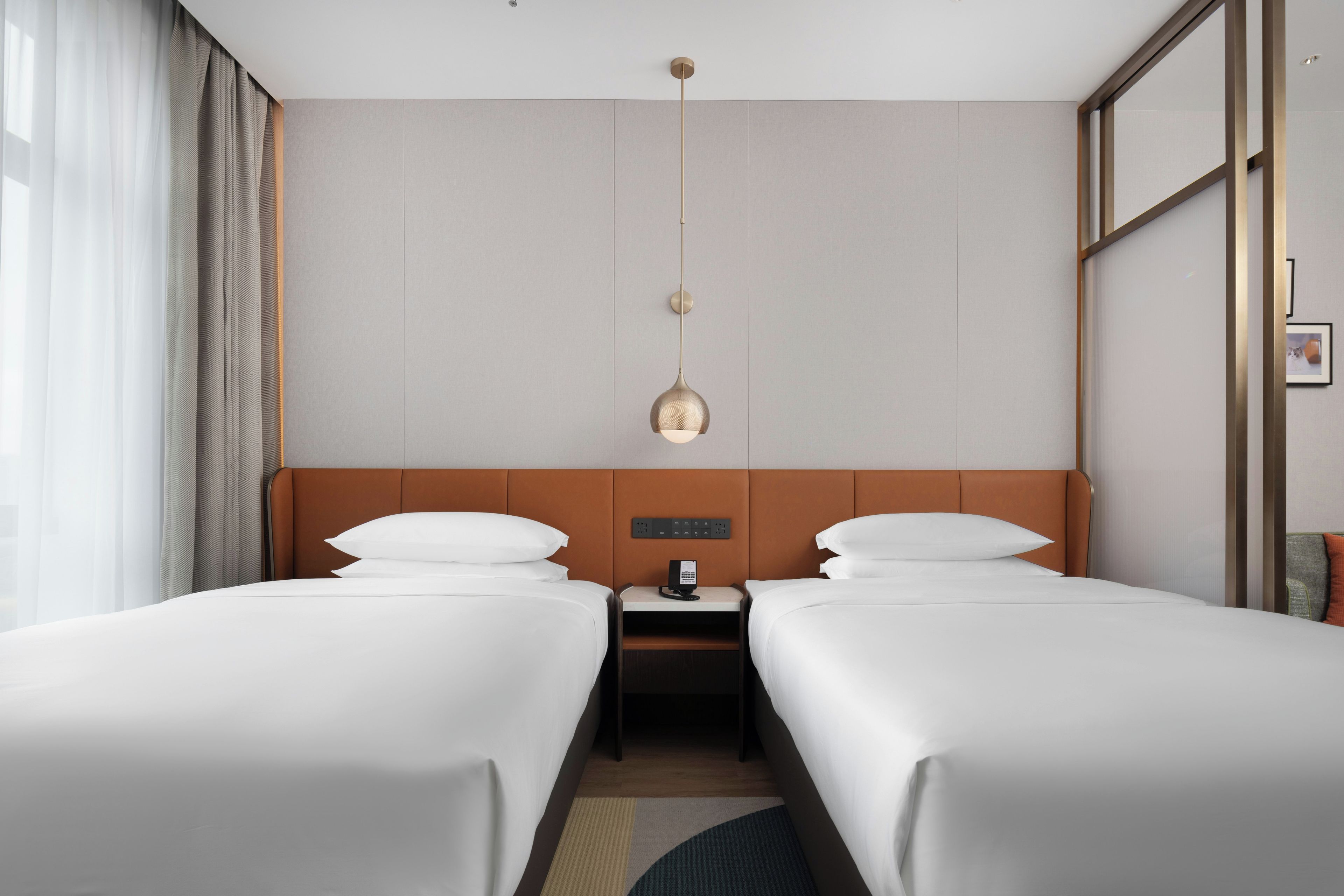 Habitación de hotel con dos camas, una mesita de noche, un teléfono y una lámpara fijada a la pared.