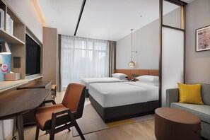 A hotel room with a bed, a desk, a chair, a sofa, and a small table.