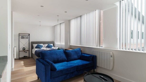 Un dormitorio moderno con un sofá azul, una cama, una mesita y un radiador.