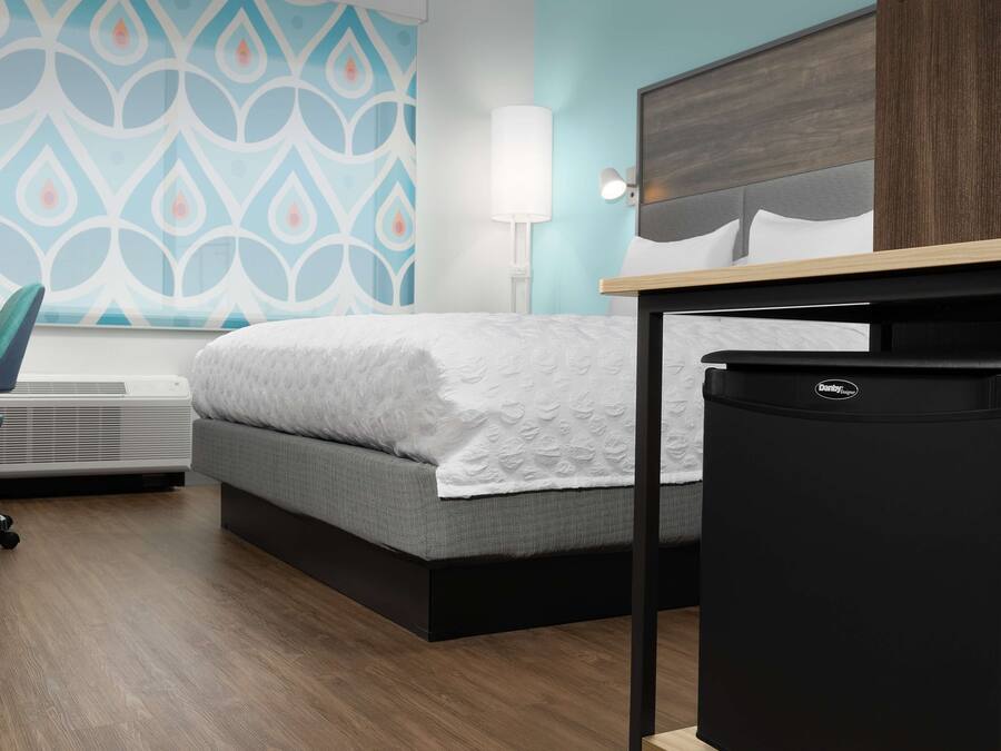 A hotel room with a bed, a desk, a chair, a lamp, and a refrigerator.