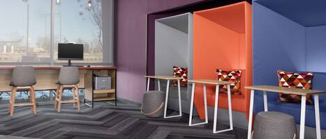 Un espace de bureau moderne doté d’une grande fenêtre, de deux bureaux avec chaises et d’un mur de séparation aux couleurs vives.