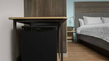 Une petite chambre comprenant un lit, un petit réfrigérateur noir et une table en bois.