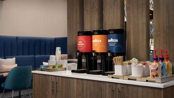 Zona de recepción de un hotel con mostrador, máquinas de café y un área de descanso con un sofá azul.