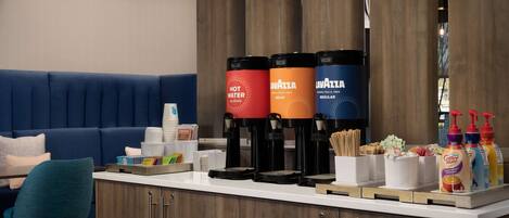 A hotel reception area with a counter, coffee makers, and a seating area with a blue couch.