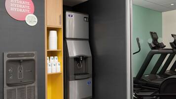 Een kitchenette met een koelkast, een waterdispenser en een plank met bekers.