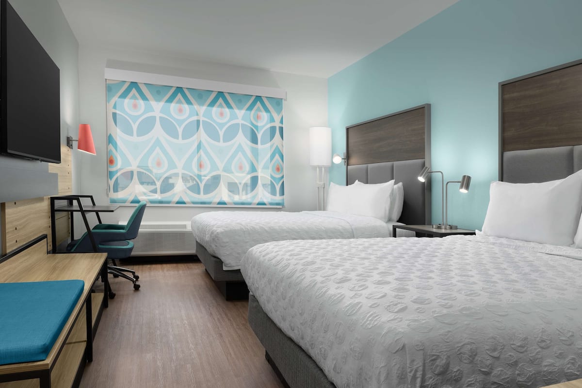 A hotel room with two beds, a desk, a chair, and a TV.
