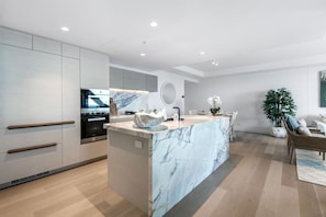 A modern kitchen with a marble island, built-in appliances, and a dining area with a wicker chair and a potted plant. - Jewel Stunning Ocean Views 2 Bed Apartment (Surfers Paradise)