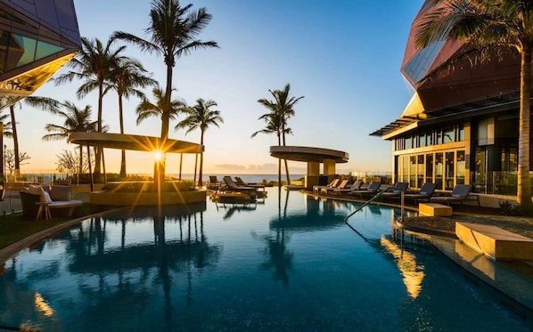 A pool area with lounge chairs and palm trees, surrounded by modern architecture. - Jewel Stunning Ocean Views 2 Bed Apartment (Surfers Paradise)