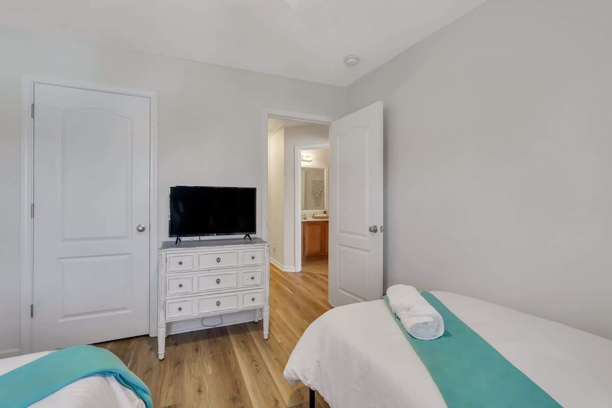 A hotel room with two beds, a TV on a dresser, and a bathroom visible through an open door.
