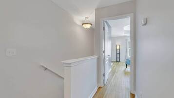 A hallway with white walls, a wooden floor, and a ceiling light fixture.