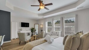 Una habitación de hotel moderna con una cama grande, un ventilador de techo, un escritorio con silla, un televisor y una ventana con persianas.