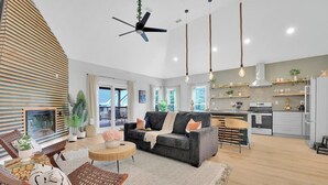 A modern living room with a sofa, coffee table, and chairs, a kitchen with a stove and shelves, and a ceiling fan. - Beautifully decorated and spacious home with a pool. (Rex)