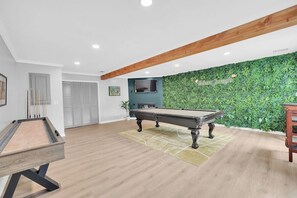 A modern indoor space with a pool table, a billiards rack, and a green wall with a jungle theme.