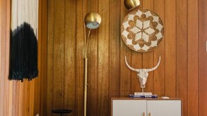 Una stanza con pareti rivestite in legno, un tappeto rotondo intrecciato, un armadietto bianco, una panca e una lampada da terra alta.