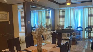 A dining area with a chandelier, a long table with chairs, and a view into the living room. - Discounted | Elegant 2BR, 2 BA Suite Beside Eastwood Mall (Quezon City)