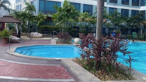 A modern hotel with a swimming pool, palm trees, and a red-tiled walkway. - Discounted | Elegant 2BR, 2 BA Suite Beside Eastwood Mall (Quezon City)