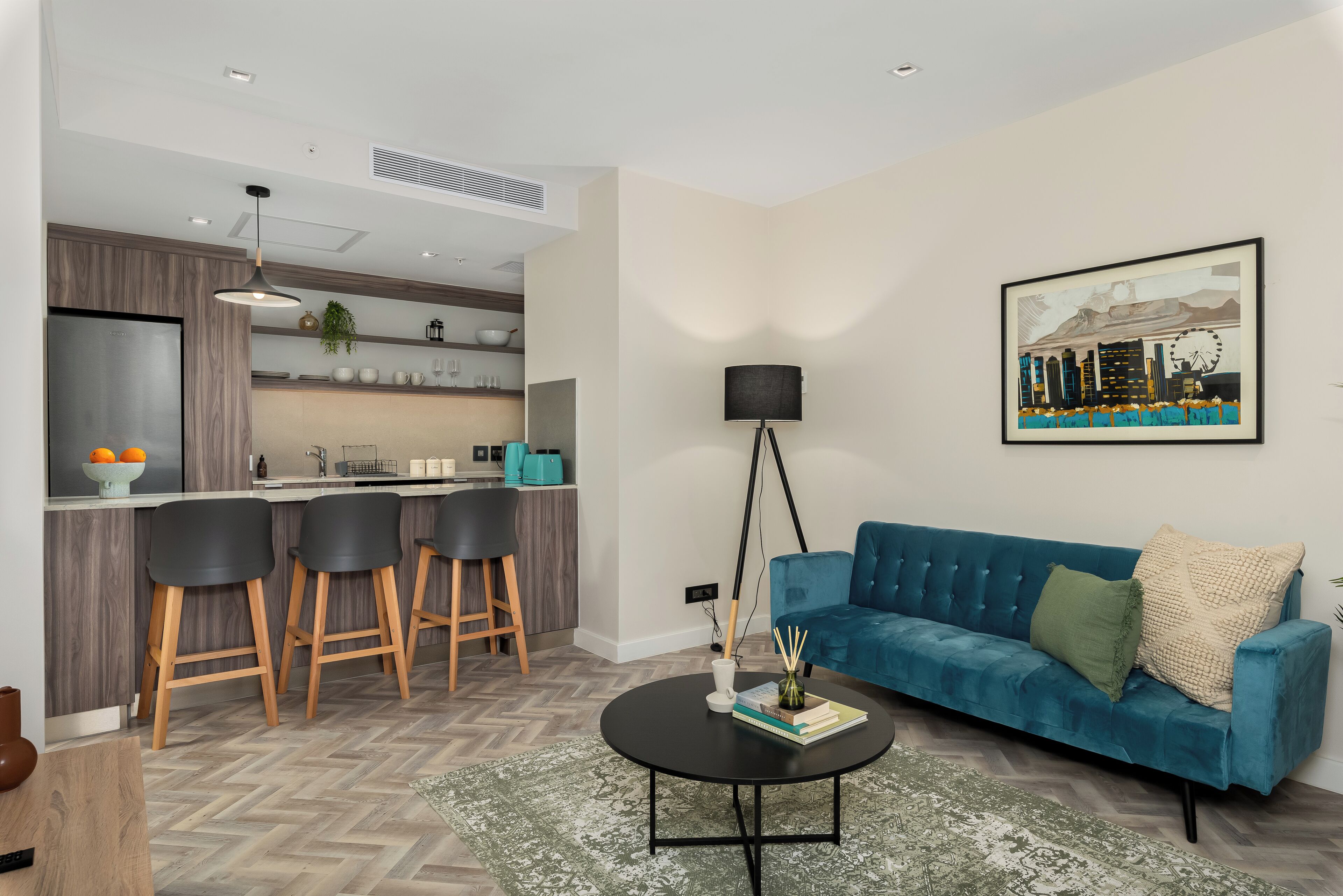 A modern living room with a blue sofa, a coffee table, and a kitchen area in the background.