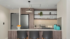 Cozinha moderna com ilha central, banquetas, luminária pendente e prateleiras embutidas com utensílios de cozinha.