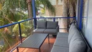 Un balcon avec un canapé gris, une petite table et une rambarde bleue.
