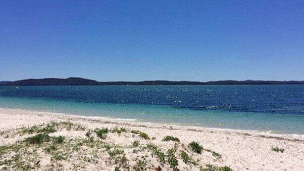 Une plage avec une eau d’un bleu limpide et un rivage sablonneux.