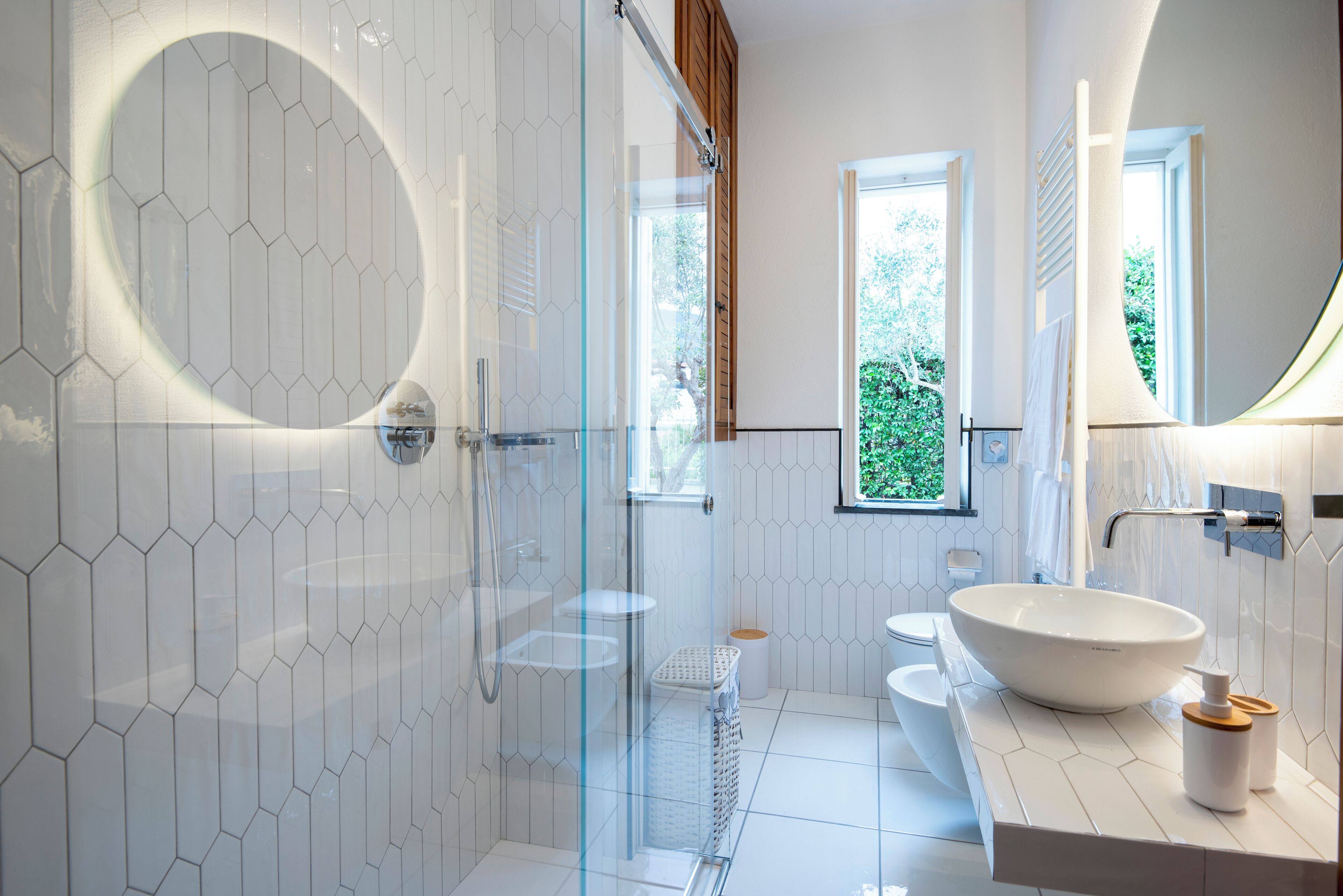 A modern bathroom with a glass-enclosed shower, a large vessel sink, and a window providing natural light.