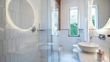 A modern bathroom with a glass-enclosed shower, a large vessel sink, and a window providing natural light.