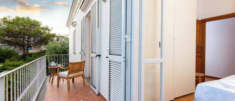 Een balkon met een stoel, een tafel, een schuifdeur en een bed in de aangrenzende kamer.