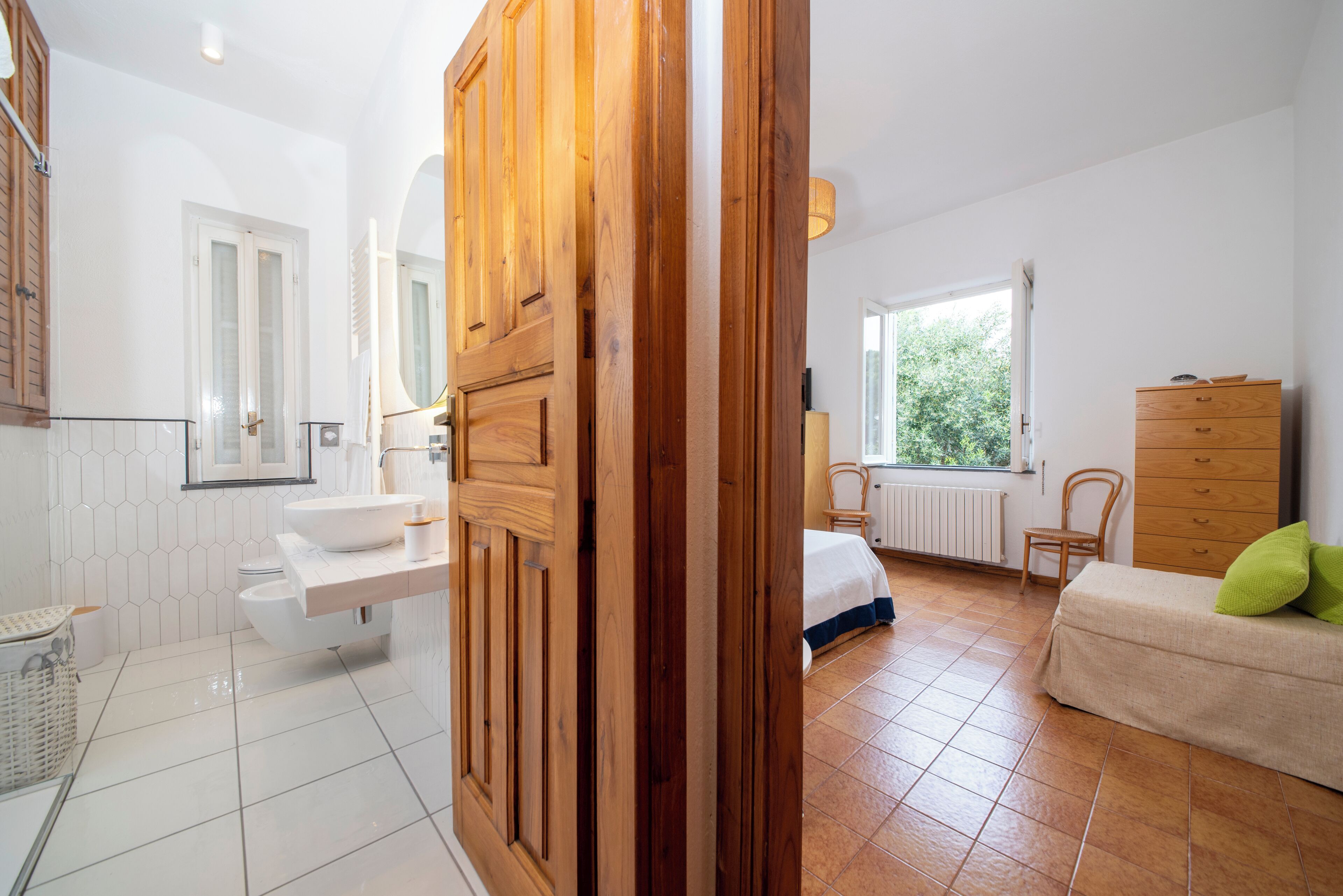A modern bathroom with a white sink, wooden door, and a window providing natural light.