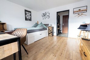 A modern bedroom with a bed, a desk, and a chair. There is a wooden floor and a white wall with a map decoration.