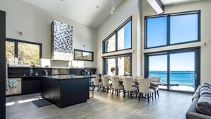 Een moderne keuken met een groot eiland, een eetgedeelte met stoelen en grote ramen met uitzicht op de oceaan.