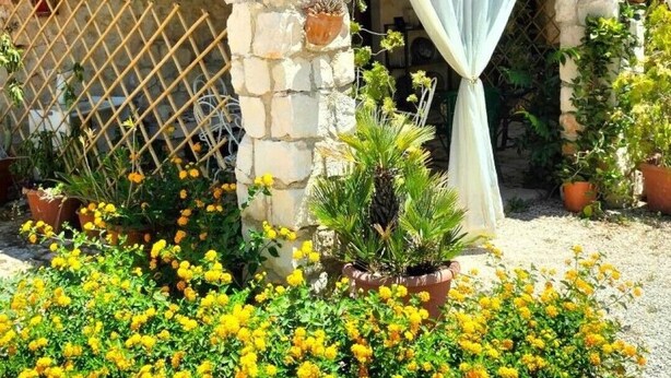 A stone building with a tiled roof, a lattice fence, and potted plants. - Torre Rodosta  (Modica)