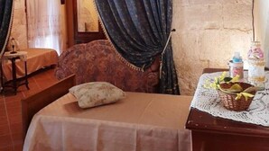 Un dormitorio con una cama, una mesita de noche de madera, una cesta de mimbre y una mesa con mantel de encaje.